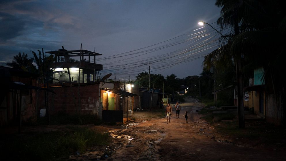 In this May 10, 2020 photo, residents walk on a dirt road in the Park of Indigenous Nations community, in Manaus, Brazil. The South American country has Latin America's highest COVID-19 death toll. The country's hardest hit major city per capita is i