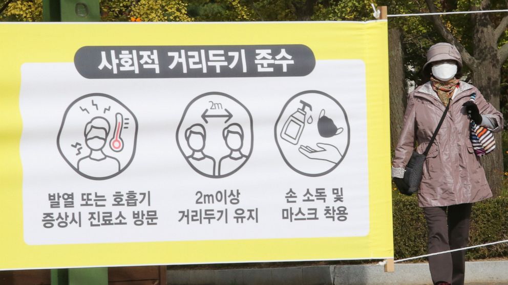 A woman wearing a face mask to help protect against the spread of the coronavirus walks by a social distancing sign at a park in Goyang, South Korea, Thursday, Oct. 15, 2020. South Korea reported more than 100 new cases of the coronavirus, half of th