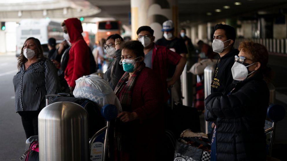 Travelers wait for a shuttle but to arrive at the Los Angeles International Airport in Los Angeles, Monday, Dec. 20, 2021. The Los Angeles County Department of Public Health reported more than 3,500 new cases of COVID-19 on Sunday as the number of da