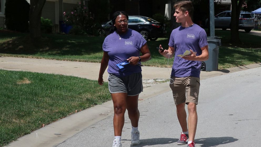 College students Alyssa Winters, left, and Ben Kennedy, right, chat as they go door-to-door to talk to prospective voters about a proposed amendment to the Kansas Constitution that would allow legislators to further restrict or ban abortion, Friday, 