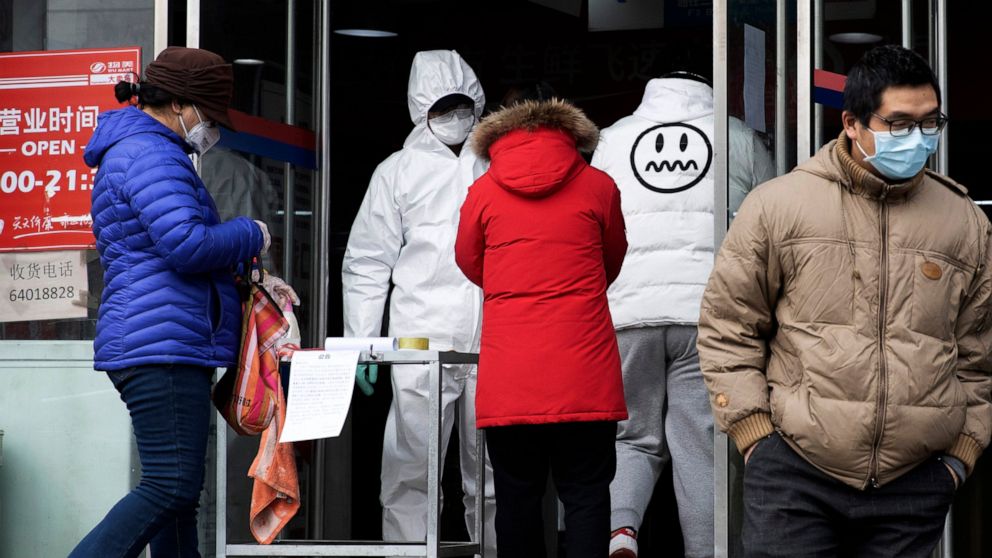 FILE - In this Thursday, Feb. 27, 2020, file photo, a worker in overalls screen for fever at the entrance to a supermarket in Beijing. Health officials reported the first U.S. drug shortage tied to the viral outbreak that is disrupting production in 