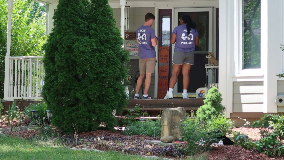 Ben Kennedy, left, and Alyssa Winters, left, wait at a door to speak with prospective voters about a proposed amendment to the Kansas Constitution that would allow legislators to further restrict or ban abortion, Friday, July 8, 2022, in Olathe, Kan.