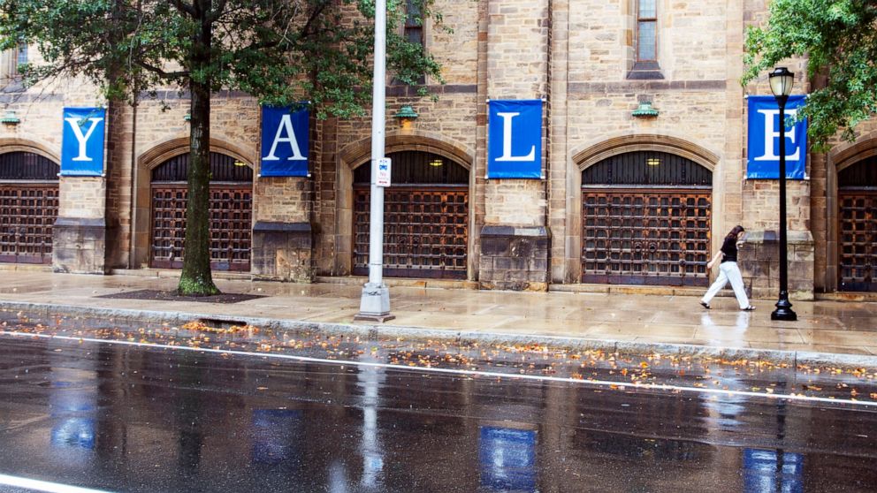 FILE - A woman walks by a Yale sign reflected in the rainwater in the street on the Yale University campus in New Haven, Conn., Aug. 22, 2021. Yale University is being accused in a federal lawsuit filed Wednesday, Nov. 30, 2022, of discriminating aga
