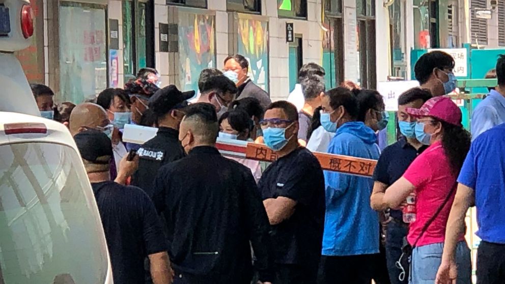 Police and security officials watch as people gather at a coronavirus testing center at a sports facility in Beijing, Tuesday, June 16, 2020. China reported several dozen more coronavirus infections Tuesday as it increased testing and lockdown measur