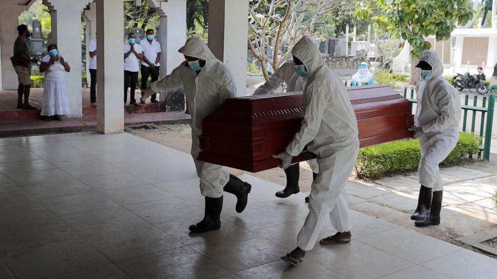 Sri Lankan health workers carry a coffin carrying remains of a COVID -19 victim to a cremation furnace as relatives watch from a distance in Colombo, Sri Lanka, Wednesday, Feb. 10, 2021. (AP Photo/Eranga Jayawardena)