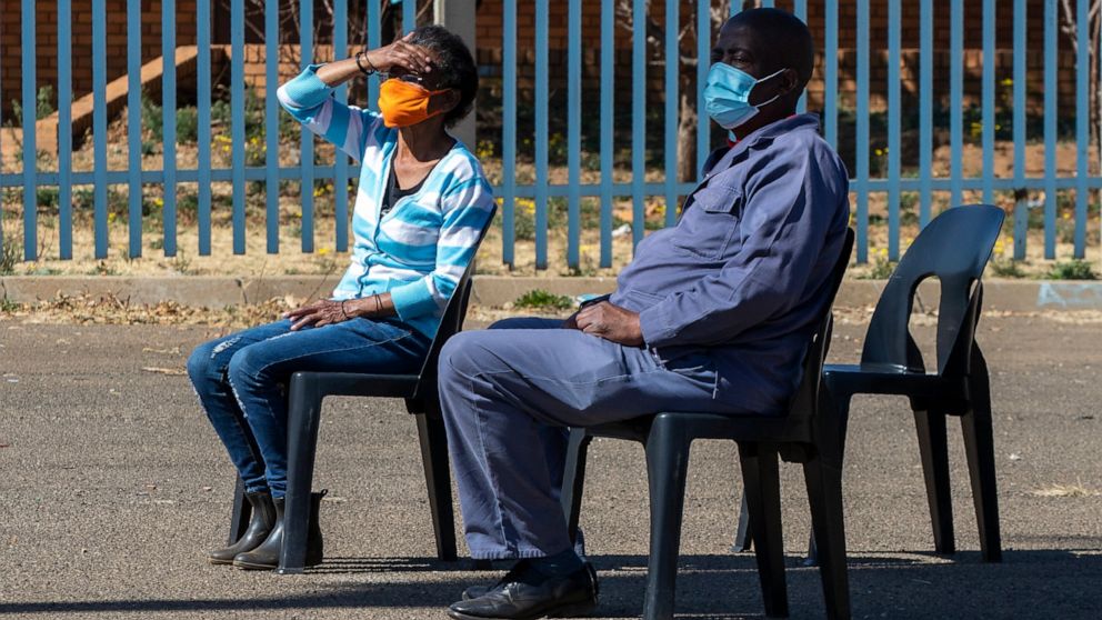 People wearing face masks to protect against coronavirus, sit on chairs whilst queuing to be screened and tested for COVID-19 in Eldorado Park outside of Johannesburg, South Africa, Monday, Aug. 3, 2020. (AP Photo/Themba Hadebe)