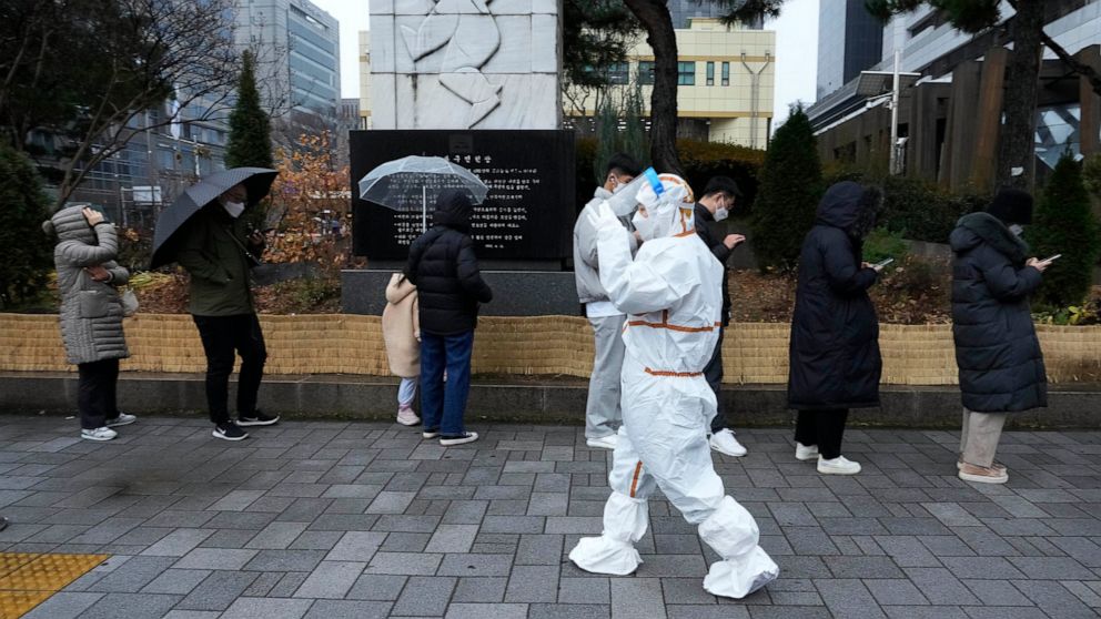 A medical workers passes by people as they wait for the coronavirus testing outside a public health center in Seoul, South Korea, Wednesday, Dec. 15, 2021. Halting its steps toward normalcy, South Korea will clamp down on social gatherings and cut th