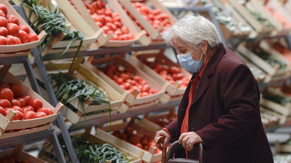 An elderly lady wearing a mask for protection against COVID-19 infection looks at vegetables after the opening of a market selling Romanian food products discounted by 25 percent for pensioners and 15 percent for students living or studying in the di