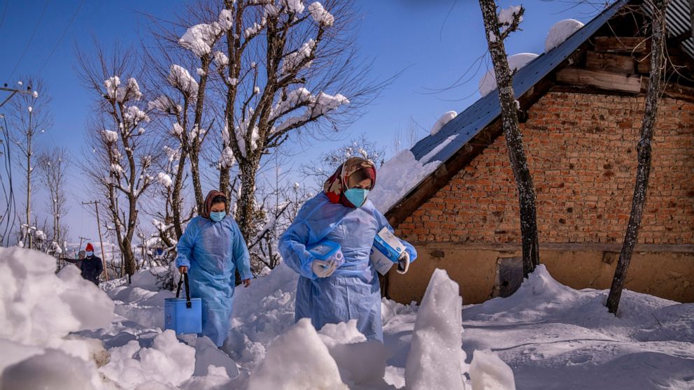 Fozia, right and Tasleema, Kashmiri healthcare workers, carry vaccines as they walk on a snow covered road during a COVID-19 vaccination drive in Budgam, southwest of Srinagar, Indian controlled Kashmir, Jan. 11, 2022. (AP Photo/Dar Yasin)