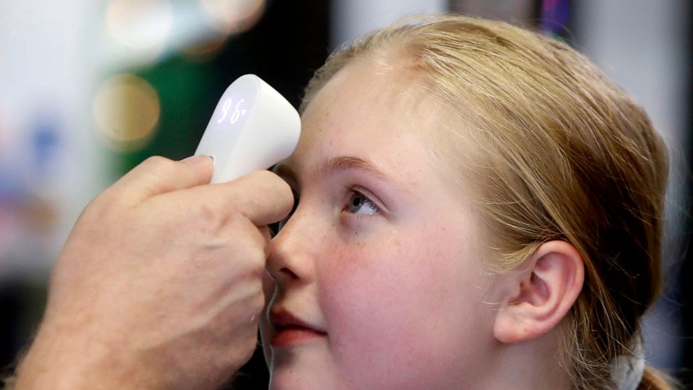 FILE - In this May 19, 2020, file photo, Kaiden Melton, 12, has her temperature taken during a daycare summer camp at Legendary Blackbelt Academy in Richardson, Texas. Coronavirus cases are rising in nearly half the U.S. states, as states are rolling