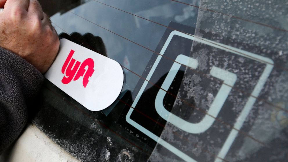 FILE- In this Jan. 31, 2018, file photo, a Lyft logo is installed on a Lyft driver's car next to an Uber sticker in Pittsburgh. On Monday, Aug. 10, 2020, a California judge ordered ride-hailing companies Uber and Lyft to treat their drivers as employ
