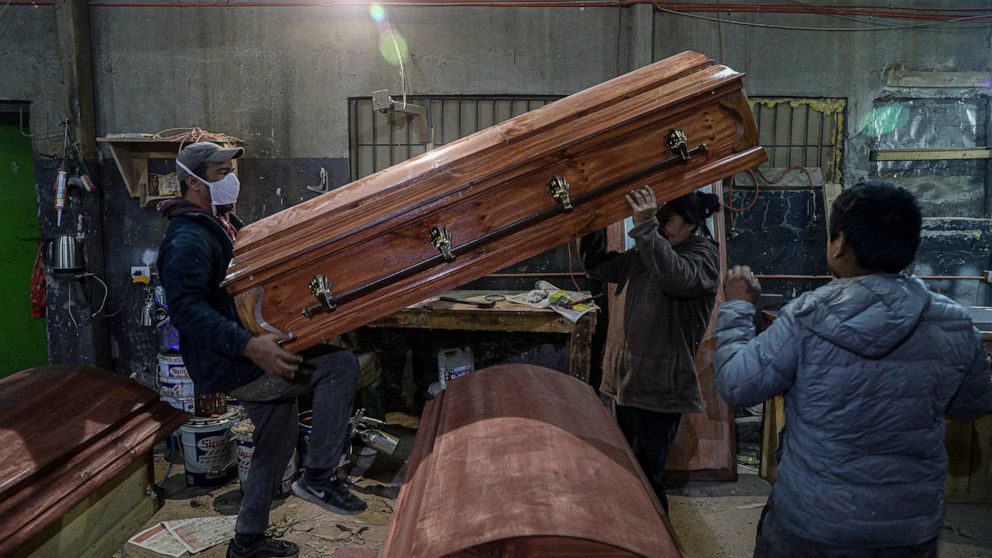 Coffin makers lift a casket at the Bergut Funeral Services factory in Santiago, Chile, Thursday, June 18, 2020. The coffin production has had to increase up to 120%, according to Nicolas Bergerie, owner of the factory. His more basic coffin model is 