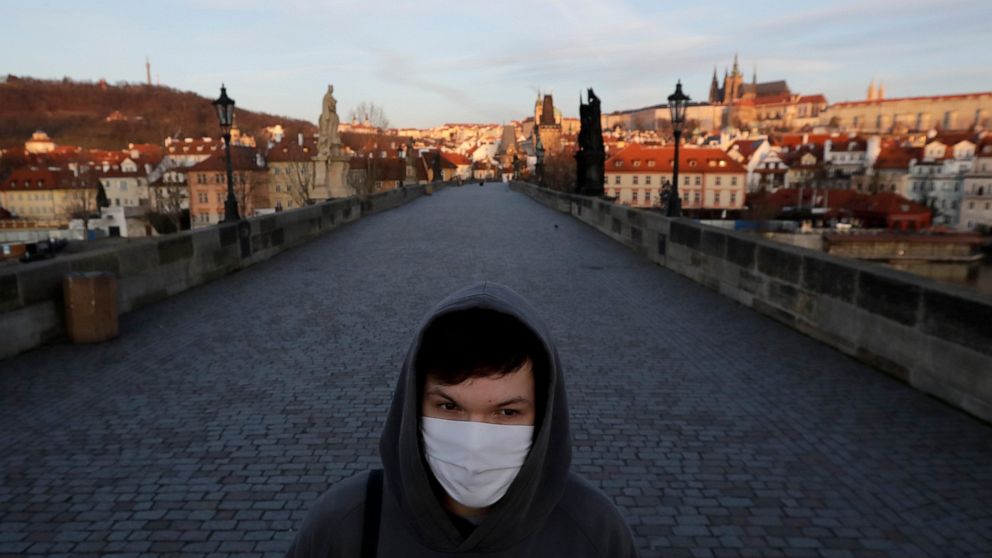 FILE - In this March 16, 2020 file photo a young man wearing a face mask walks across an empty Charles Bridge in Prague, Czech Republic. The Czech Republic has been hit by a steep rise in COVID-19 infections that have reached the levels unseen since 