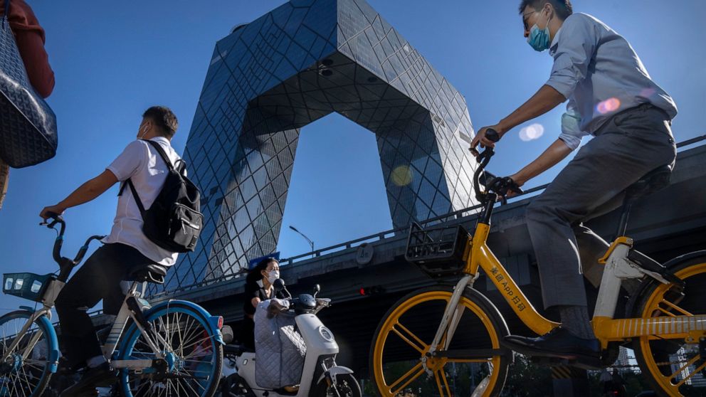 Commuters wearing face masks ride bicycles near the China Central Television (CCTV) building in the central business district in Beijing, Thursday, Sept. 1, 2022. (AP Photo/Mark Schiefelbein)