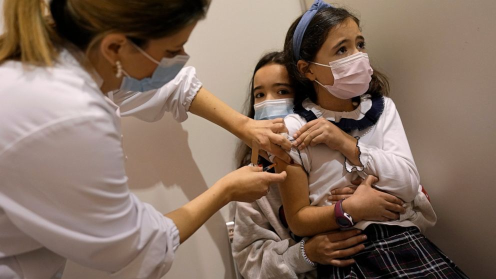 FILE - Maria do Carmo, 8, sits on the lap of her sister Madalena, 11, while nurse Catarina administers a dose of the vaccine against COVID-19, Dec. 18, 2021. Despite vaccination rates that make other governments envious, Spain and Iberian neighbor Po