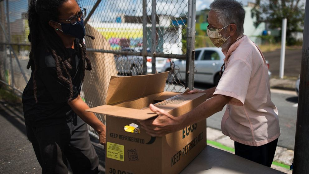 Manuel Berrios, right, takes a food donation from Giovanni Roberto, coordinator of Comedores Sociales (Social Canteens) a non-profit entity dedicated to offering hot meals in the middle of the Covid-19 pandemic, in Caguas, Puerto Rico, Wednesday, Apr