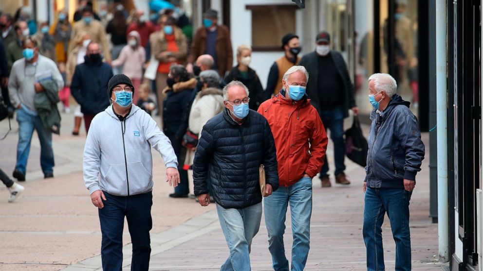 People wearing masks walk down a street in Saint Jean de Luz, southwestern France, Monday, Oct. 12, 2020. Some parts of France have been put on maximum coronavirus alert level, which means shutting down bars, implementing stricter measures in restaur