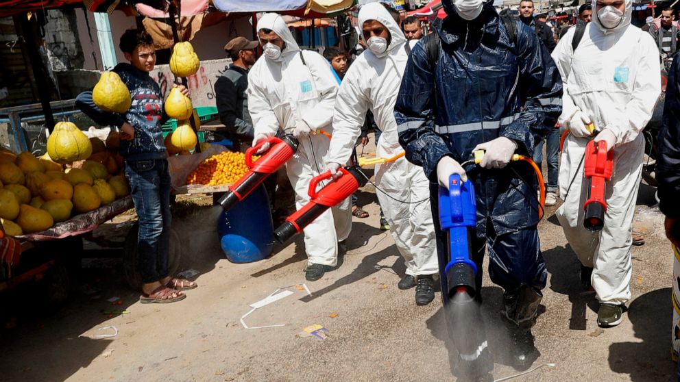 Workers wearing protective gear spray disinfectant as a precaution against the coronavirus, at the main market in Gaza City, Thursday, March 19, 2020. The Middle East has some 20,000 cases of the virus, with most cases in Iran or linked to travel fro