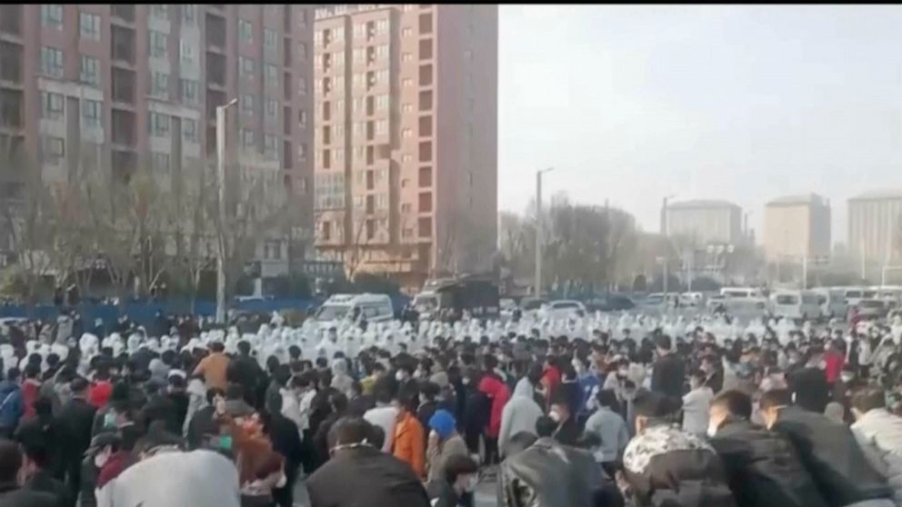 In this photo provided Nov 23, 2022, protesters face off against security personnel in white protective clothing at the factory compound operated by Foxconn Technology Group who runs the world's biggest Apple iPhone factory in Zhengzhou in central Ch