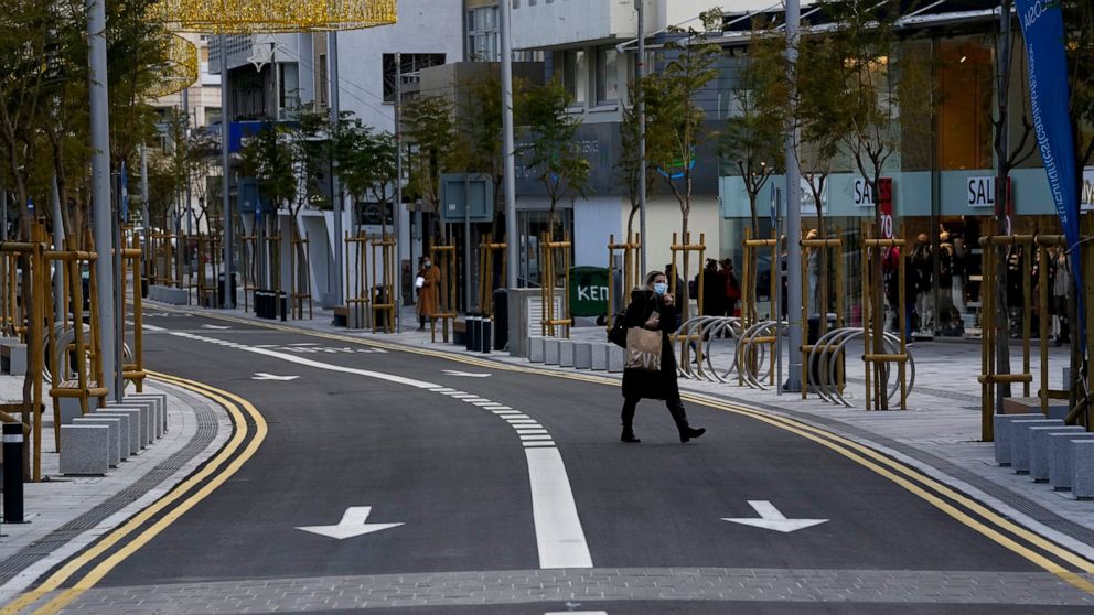 A woman wearing a protective mask walks at a main shopping street in central capital Nicosia, Cyprus, Wednesday, Jan. 19, 2022. Tourism-reliant Cyprus will lift a requirement for all inbound travelers to either show a negative COVID-19 test or to sel