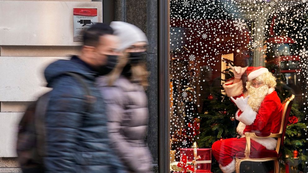 A man dressed as Santa Claus gestures as people walk past, in London, Saturday, Dec. 4, 2021. Britain says it will offer all adults a booster dose of vaccine within two months to bolster the nation's immunity as the new omicron variant of the coronav
