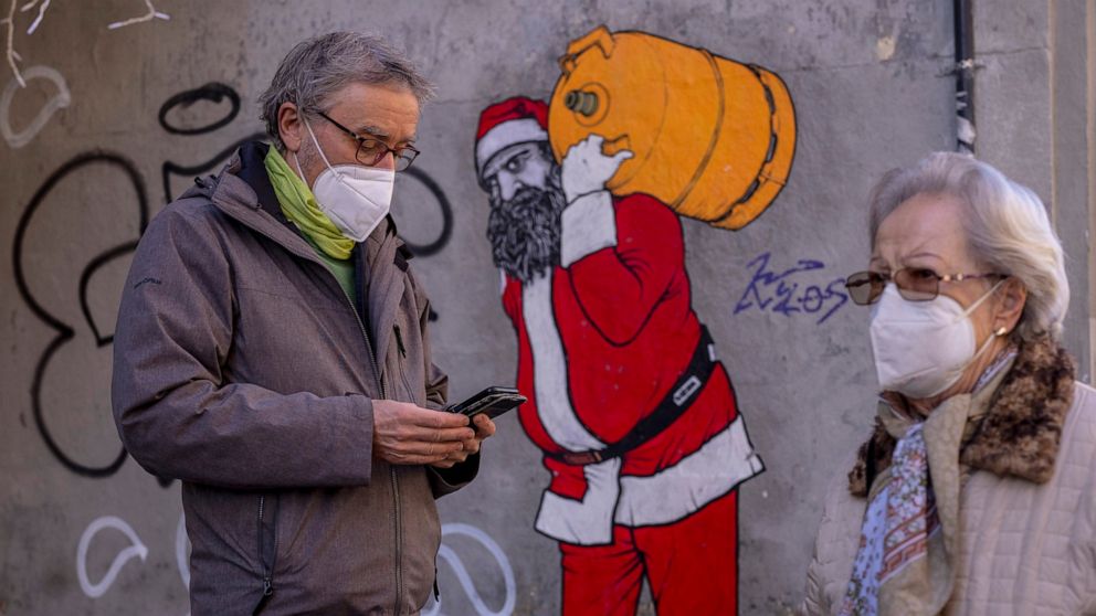 A man and woman wearing FFP2 masks to curb the spread of COVID-19 are seen in front of a mural depicting Santa Claus, in Madrid, Spain, Wednesday, Jan. 12, 2022. Italy, Spain and other European countries are re-instating or stiffening mask mandates a
