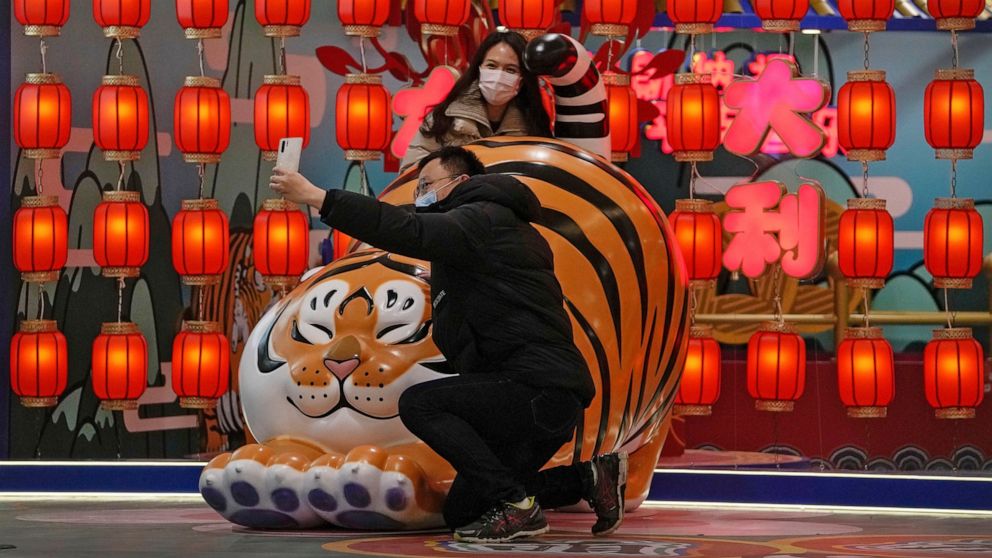 A couple wearing face masks to protect from the coronavirus take a selfie with a tiger decoration, a Chinese zodiac which marks the year 2022, at a shopping mall in Beijing, Sunday, Jan. 9, 2022. Tianjin, a major Chinese port city near the capital Be