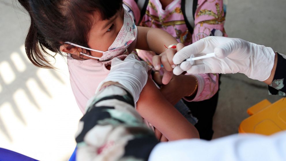 A young girl held by her mother pushes a shaft of a needle as she receives a first dose of Sinovac's COVID-19 vaccine at a health center outside Phnom Penh, Cambodia on Wednesday, Feb. 23, 2022. Cambodia began vaccinating 3- and 4-year-olds with Chin