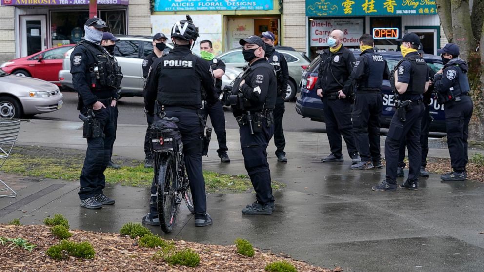 FILE - Seattle Police officers confer after taking part in a public roll call at Hing Hay Park in Seattle's Chinatown-International District Thursday, March 18, 2021. Seattle's police department is having detectives and non-patrol staff respond to em