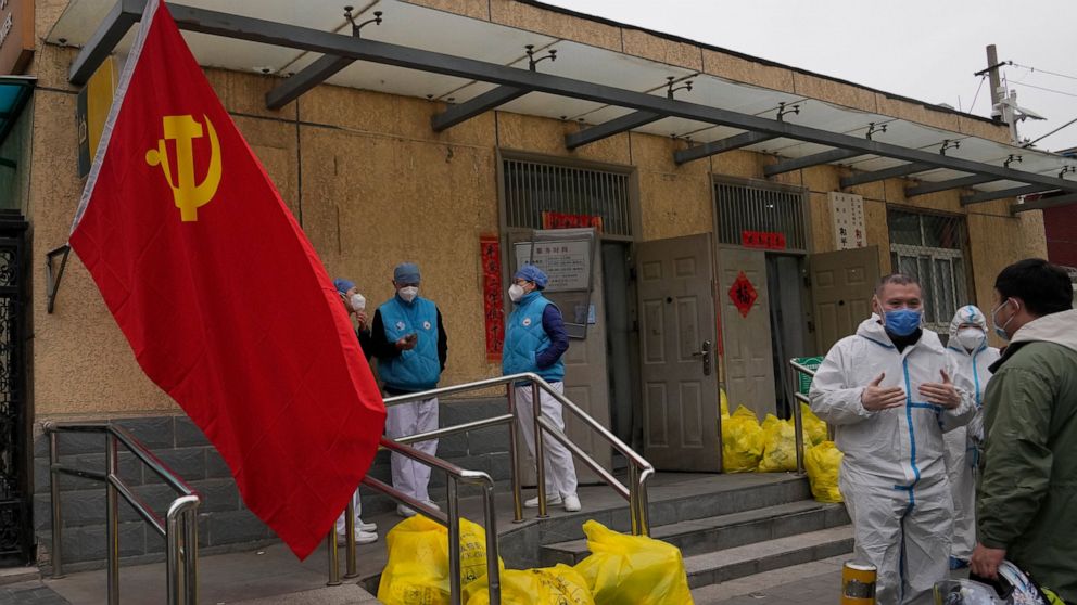 Community workers outside a locked down community chat near a Communist Party flag and trash bags labelled as hazardous waste on Thursday, March 17, 2022, in Beijing. Even as authorities lock down cities in China's worst outbreak in two years, they a