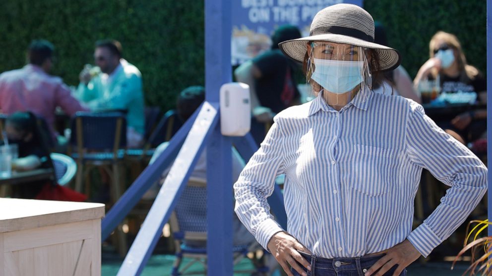 A hostess waits to sit customers on a restaurant at the pier Sunday, July 12, 2020, in Santa Monica, Calif., amid the coronavirus pandemic. A heat wave has brought crowds to California's beaches as the state grappled with a spike in coronavirus infec
