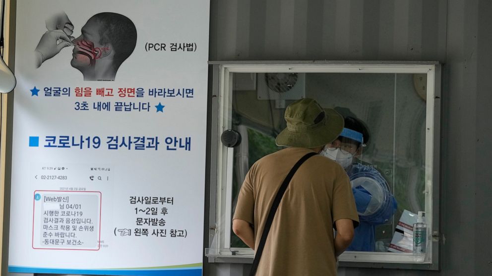 A medical worker in a booth takes a nasal sample from a man at a coronavirus testing site in Seoul, South Korea, Tuesday, July 6, 2021. The sign at left reads: "How to collect COVID-19 samples." (AP Photo/Ahn Young-joon)