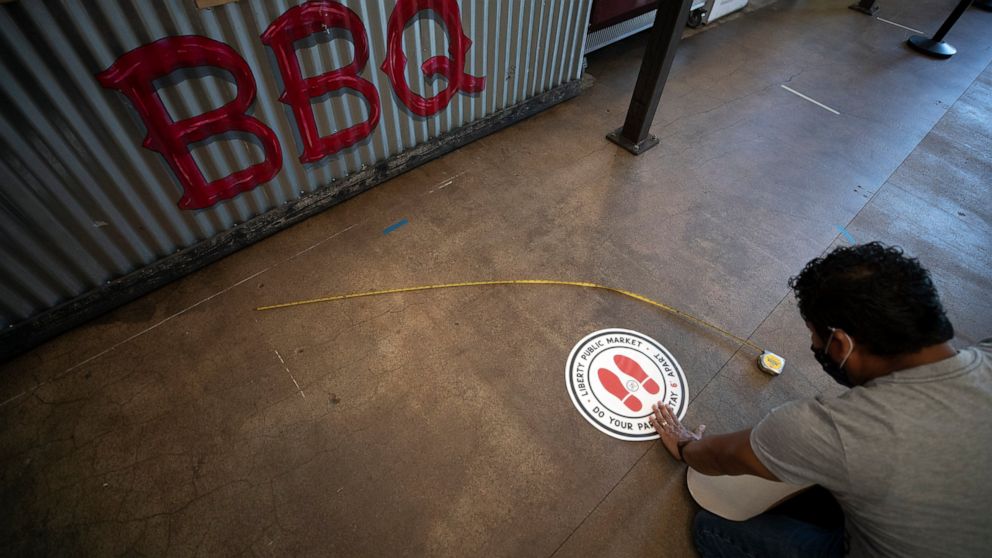 Francisco Ocampo installs a sign on the floor alerting social distancing measures at the Liberty Public Market restaurant Thursday, May 21, 2020, in San Diego. San Diego County began to relax rules regarding social distancing and efforts to slow the 