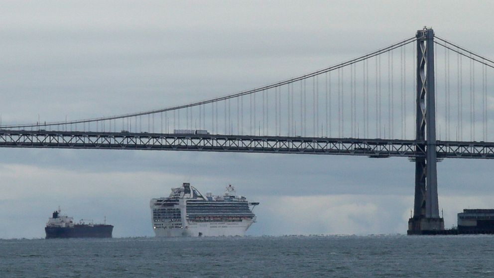 FILE - In this March 16, 2020, file photo framed by the San Francisco-Oakland Bay Bridge, the Grand Princess cruise ship makes its way to an anchorage, in San Francisco. Cruise ships are returning to San Francisco after a 19-month hiatus brought on b