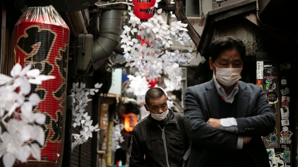 Two men wearing protective face masks walk through a narrow alleyway Monday, Jan. 27, 2020, in the Shinjuku district of Tokyo. (AP Photo/Jae C. Hong)