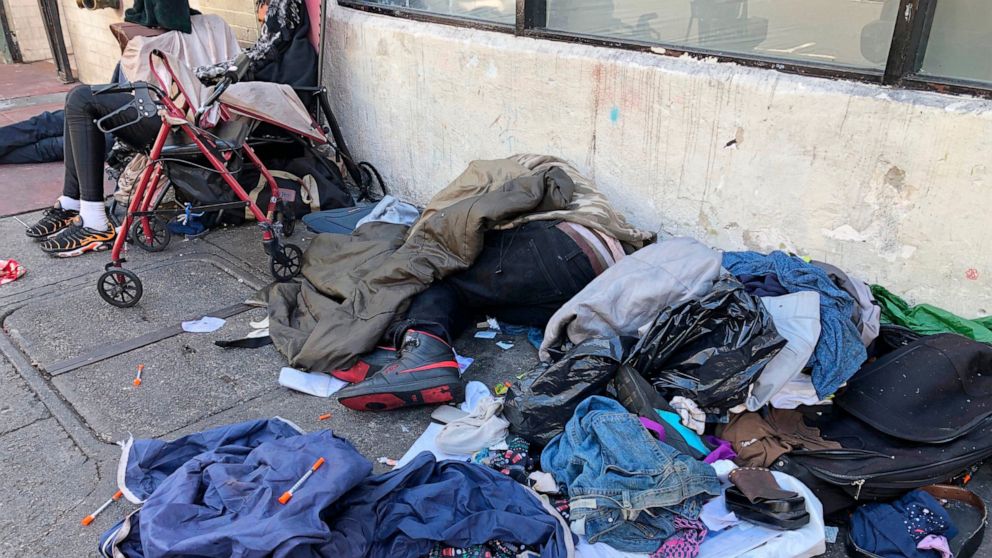 FILE - In this July 25, 2019, file photo, sleeping people, discarded clothes and used needles are seen on a street in the Tenderloin neighborhood in San Francisco. A center for people experiencing methamphetamine-induced psychosis will open in San Fr