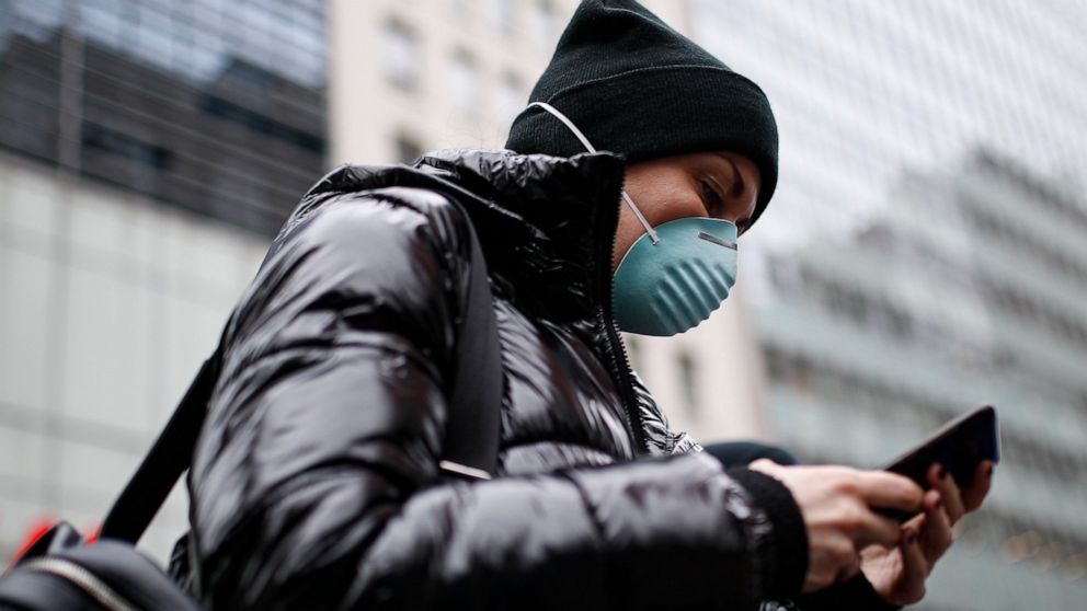 Pedestrian uses her phone while wearing a face mask in Herald Square, Thursday, March 12, 2020, in New York. New York City Mayor Bill de Blasio said Thursday he will announce new restrictions on gatherings to halt the spread of the new coronavirus in