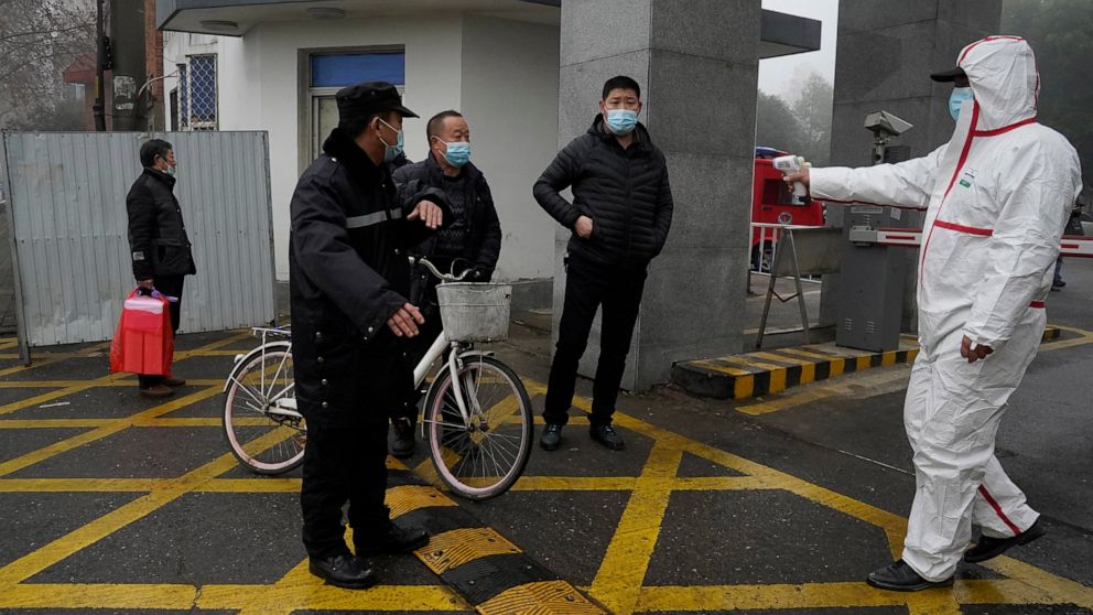 A worker in protective gear holds up a thermometer at the entrance to the Hubei Center for Disease Control and Prevention where a World Health Organization team is making a field visit in Wuhan in central China's Hubei province Monday, Feb. 1, 2021. 