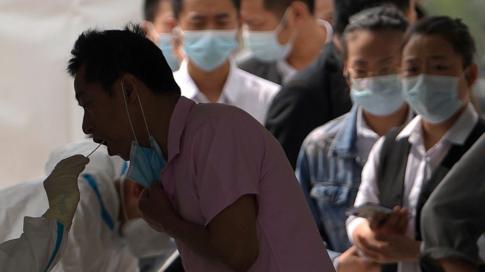 Workers line up to get a throat swab sample taken at a coronavirus test site set up near a commercial office complex, Sunday, April 24, 2022, in Beijing. Beijing is on alert after 10 middle school students tested positive for COVID-19, in what city o