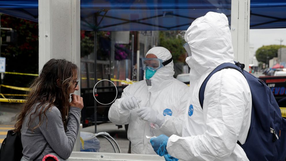 FILE - In this April 20, 2020, file photo, members of the Los Angele Fire Department wear protective equipment as they conduct a new coronavirus test on a woman, left, in the Skid Row district in Los Angeles. The city of Los Angeles will offer free c