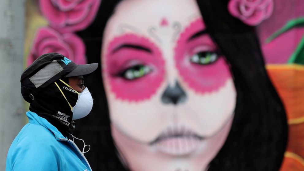 A woman wearing a face mask amid the spread of the new coronavirus walks past a Catrina mural in Bogota, Colombia, Thursday, May 21, 2020. (AP Photo/Fernando Vergara)