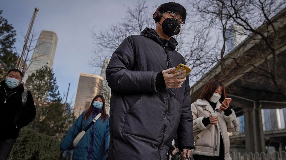 A man wearing a face mask and a disposable gloves to help curb the spread of the coronavirus heads to work with other masked people during the morning rush hour in Beijing, Monday, Jan. 11, 2012. Chinese health authorities say scores more people have