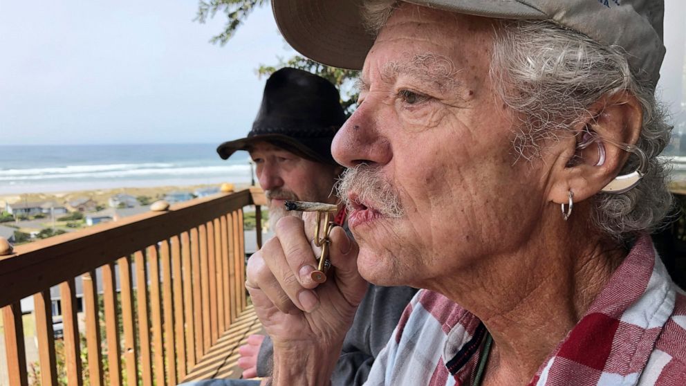 ADVANCE FOR PUBLICATION ON TUESDAY, JUNE 11, AND THEREAFTER - In this April 25, 2019, photo, two-time cancer survivor and medical marijuana cardholder Bill Blazina, 73, smokes a marijuana joint on the deck of his neighbor's home in Waldport, Ore. Bla