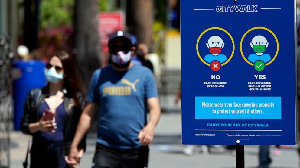 FILE - In this May 14, 2021, file photo, signs instruct visitors on the proper way to wear masks at the Universal City Walk in Universal City, Calif. California is keeping its rules for wearing facemasks in place until the state more broadly lifts it