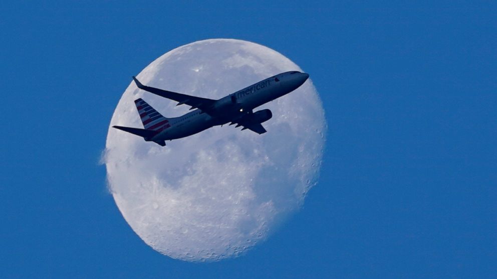 An American Airlines Boeing 737 flies past the moon as it heads to Orlando, Fla., after having taken off from Miami International Airport, Tuesday, April 19, 2022, in Miami. The major airlines and many of the busiest airports rushed to drop their req