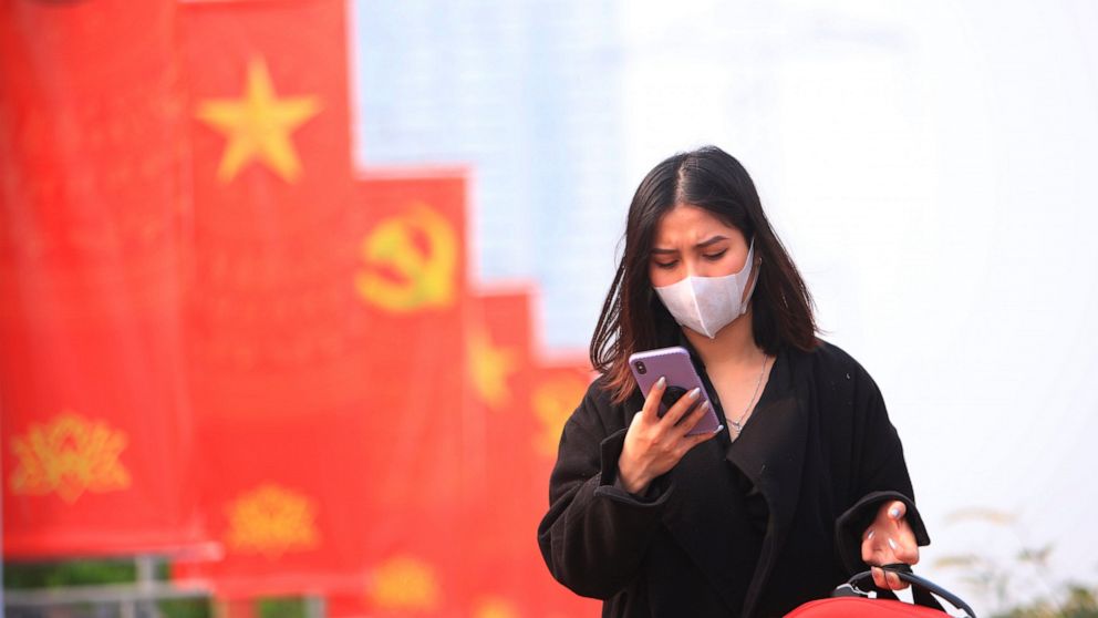FILE - In this Jan. 23, 2021 file photo, a woman wearing face mask looks at her phone in Hanoi, Vietnam. Vietnam says it has discovered a new coronavirus variant that’s a hybrid of strains first found in India and the U.K. The Vietnamese health minis