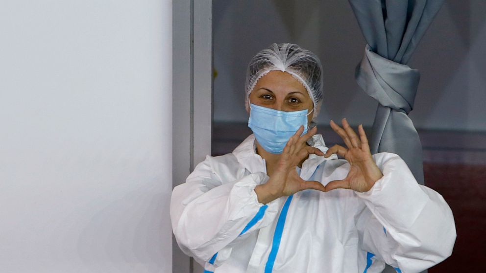 A medical worker wearing protective gear gestures as people wait to receive the COVID-19 vaccine, at Belgrade Fair makeshift vaccination center, in Belgrade, Serbia, Monday, Jan. 25, 2021. Serbia were the first European country to receive the Chinese