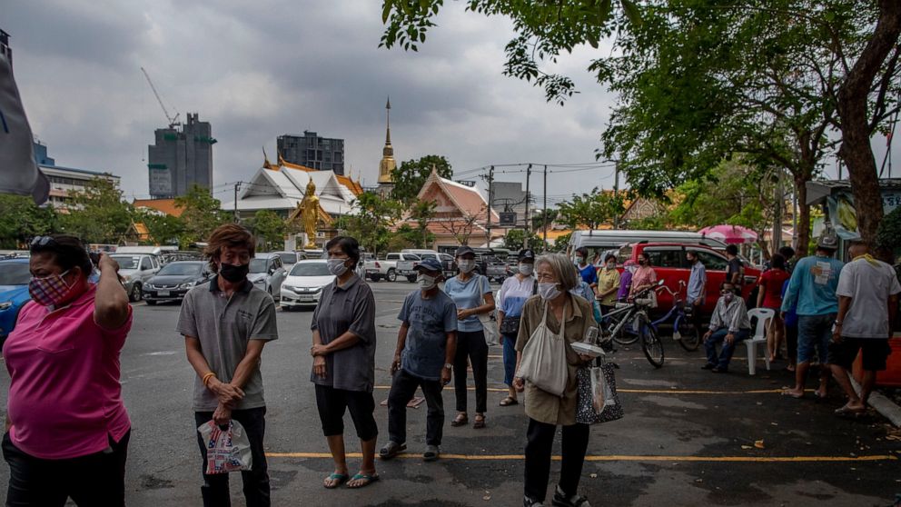 A woman, center, holds a meal as others stand in a line maintaining social distancing to receive free meals at Wat That Thong, a Buddhist temple in Bangkok, Thailand, Tuesday, April 14, 2020. Some Buddhist monasteries provide meals for people in-need
