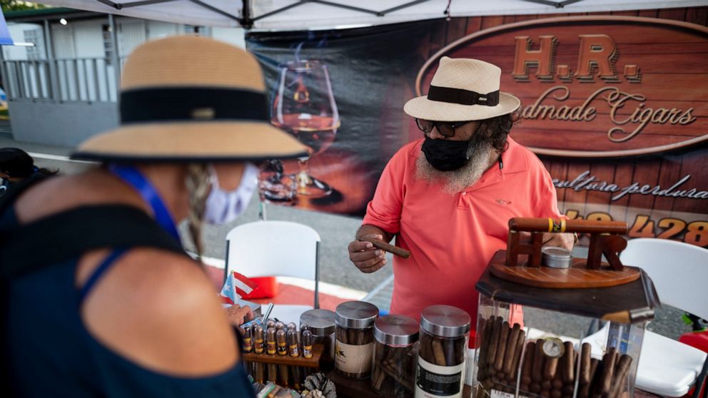 Tourists look at cigars for sale at the Old San Juan dock after the arrival of Carnival's Mardi Gras cruise ship in San Juan, Puerto Rico, Tuesday, Aug. 3, 2021, marking the first time a cruise ship visits the U.S. territory since the COVID-19 pandem