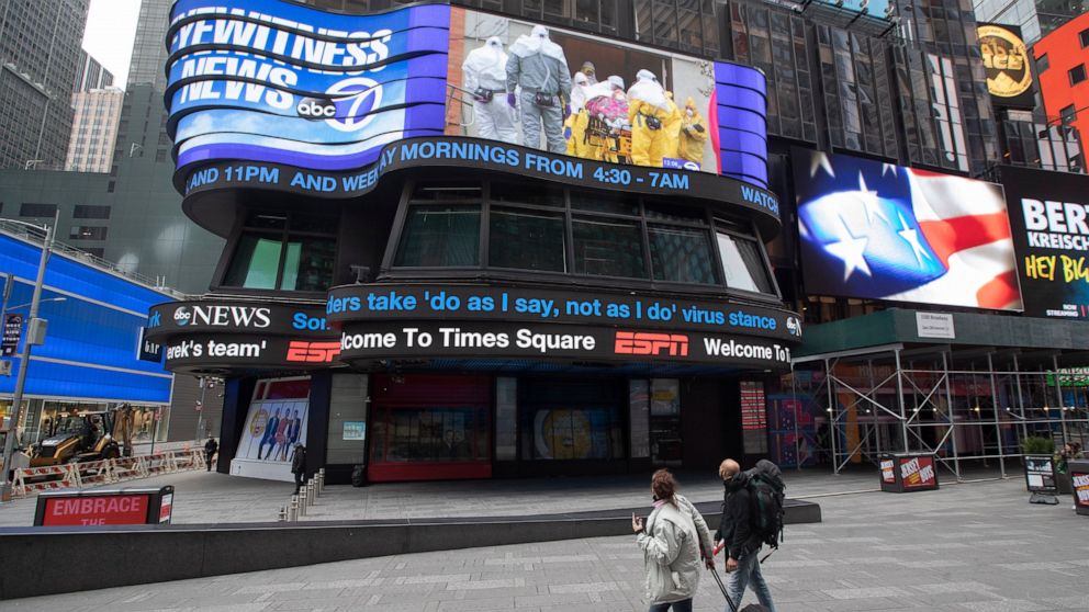 A couple looks at the ABC News video screen showing coverage of a coronavirus outbreak in Woodbridge, N.J., Wednesday, March 25, 2020, in New York's Times Square. The number of people hospitalized with COVID-19 in New York climbed to 3,800, with clos